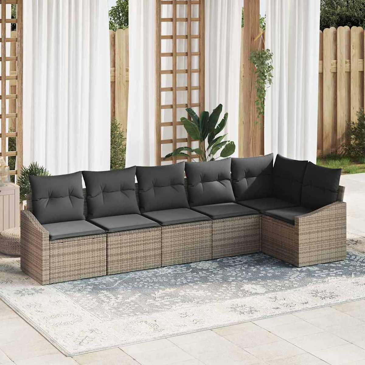 Ecksofa im Freien mit grauen Kissen auf einem gemusterten Teppich. Weiße Vorhänge und hölzerner Spalier im Hintergrund. Pflanzen sichtbar.
