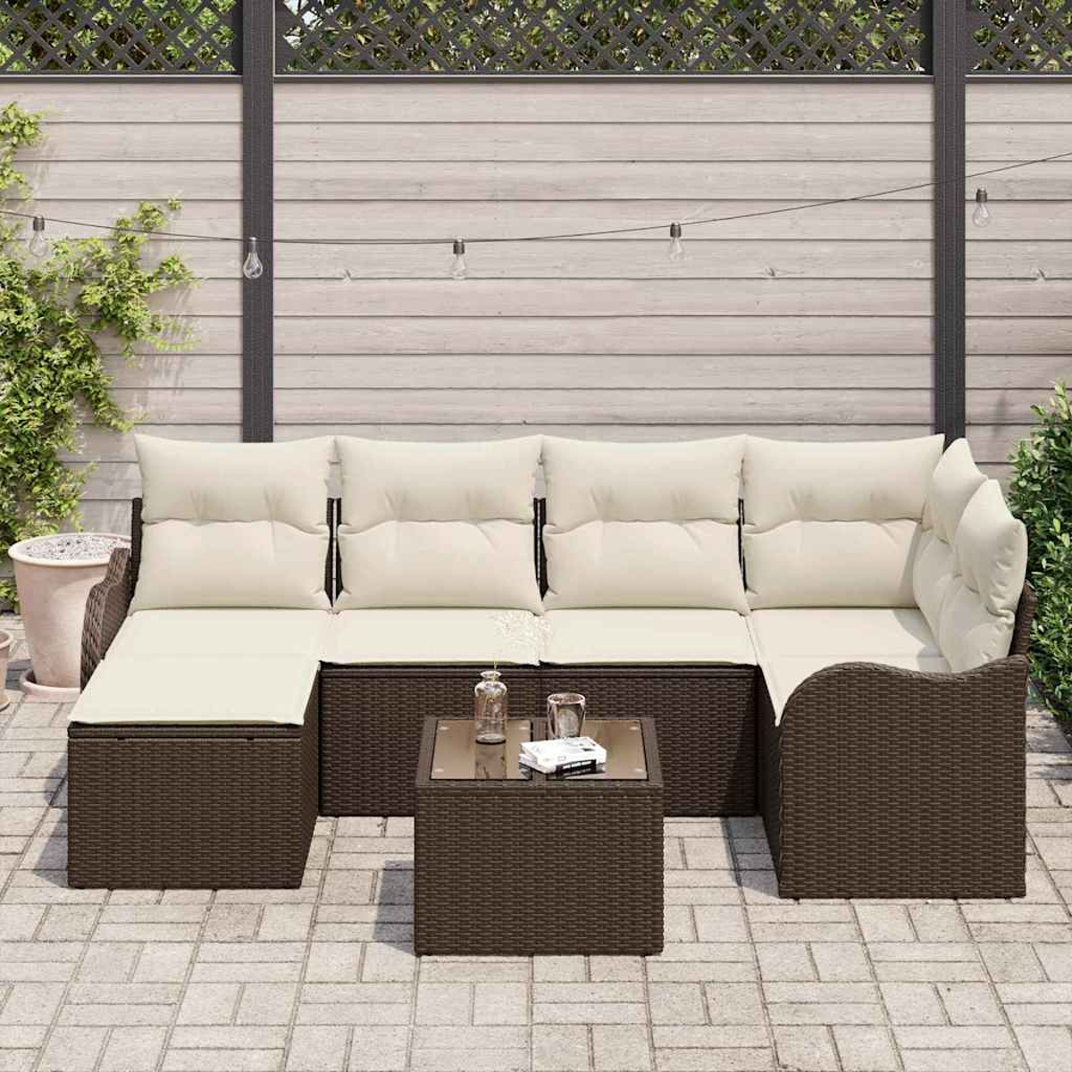 Outdoor-Ecksofa mit cremefarbenen Kissen und einem quadratischen Couchtisch. Auf einer Backstein-Terrasse, mit Holzzaun im Hintergrund.