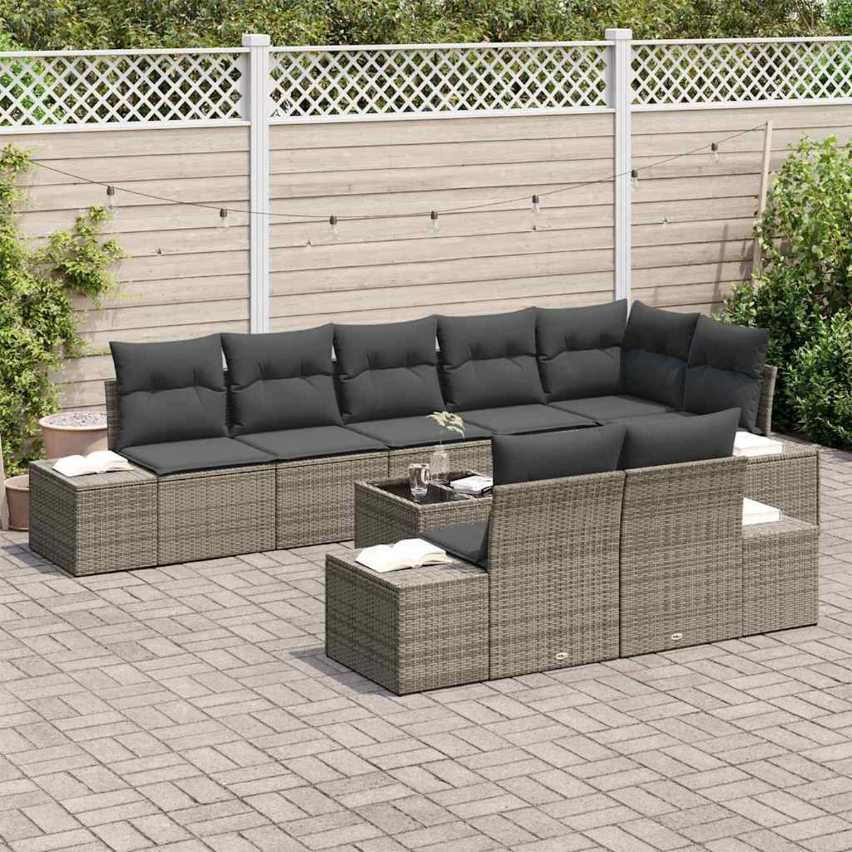 Graues Outdoor-Wicker-Sofaset mit dunkelgrauen Kissen, einem kleinen Tisch und einem weißen Zaun im Hintergrund auf einer Ziegelterrasse.