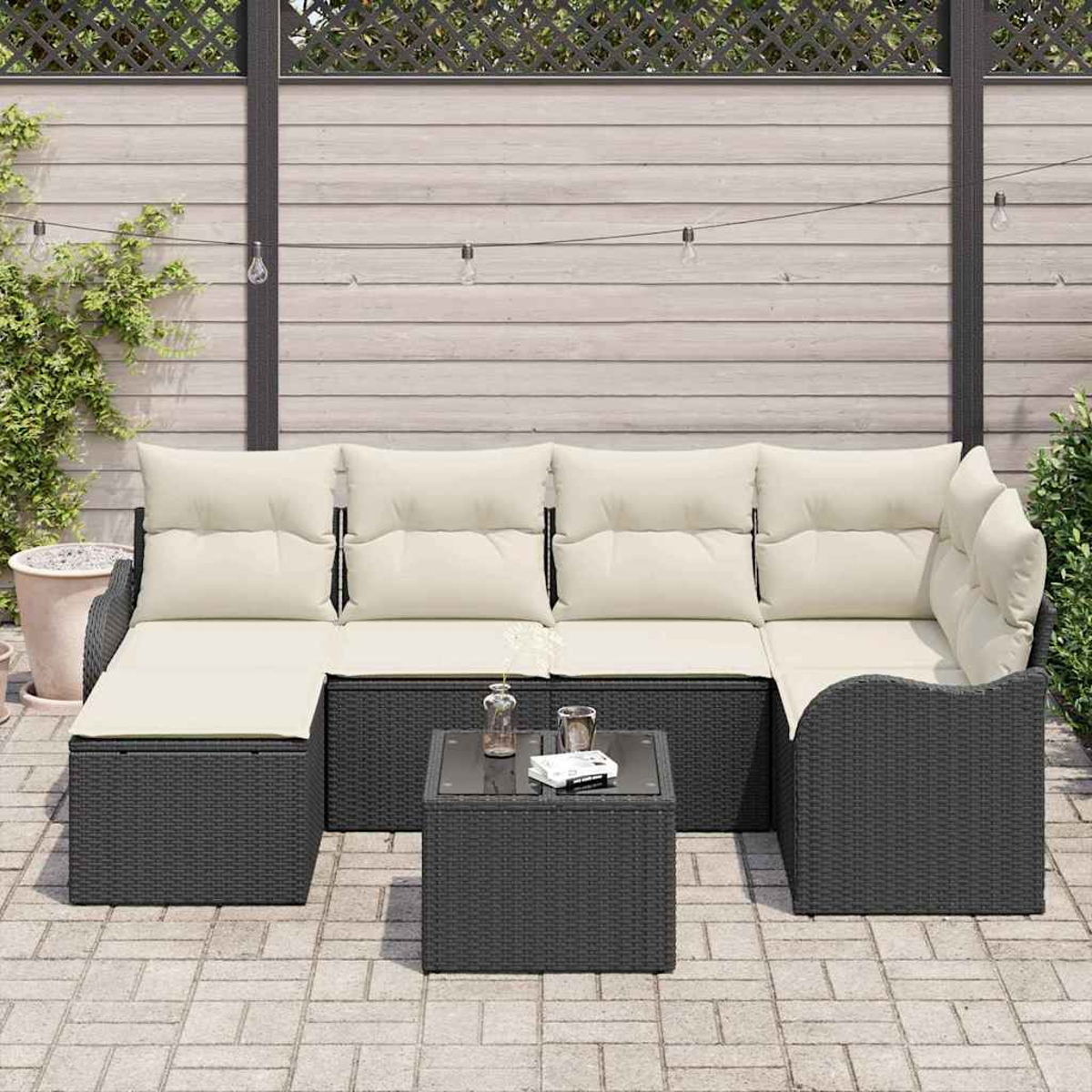 Outdoor-Ecksofa mit cremefarbenen Kissen und einem kleinen Tisch. Die Szene spielt auf einer Terrasse mit Holzzaun und Lichterketten.