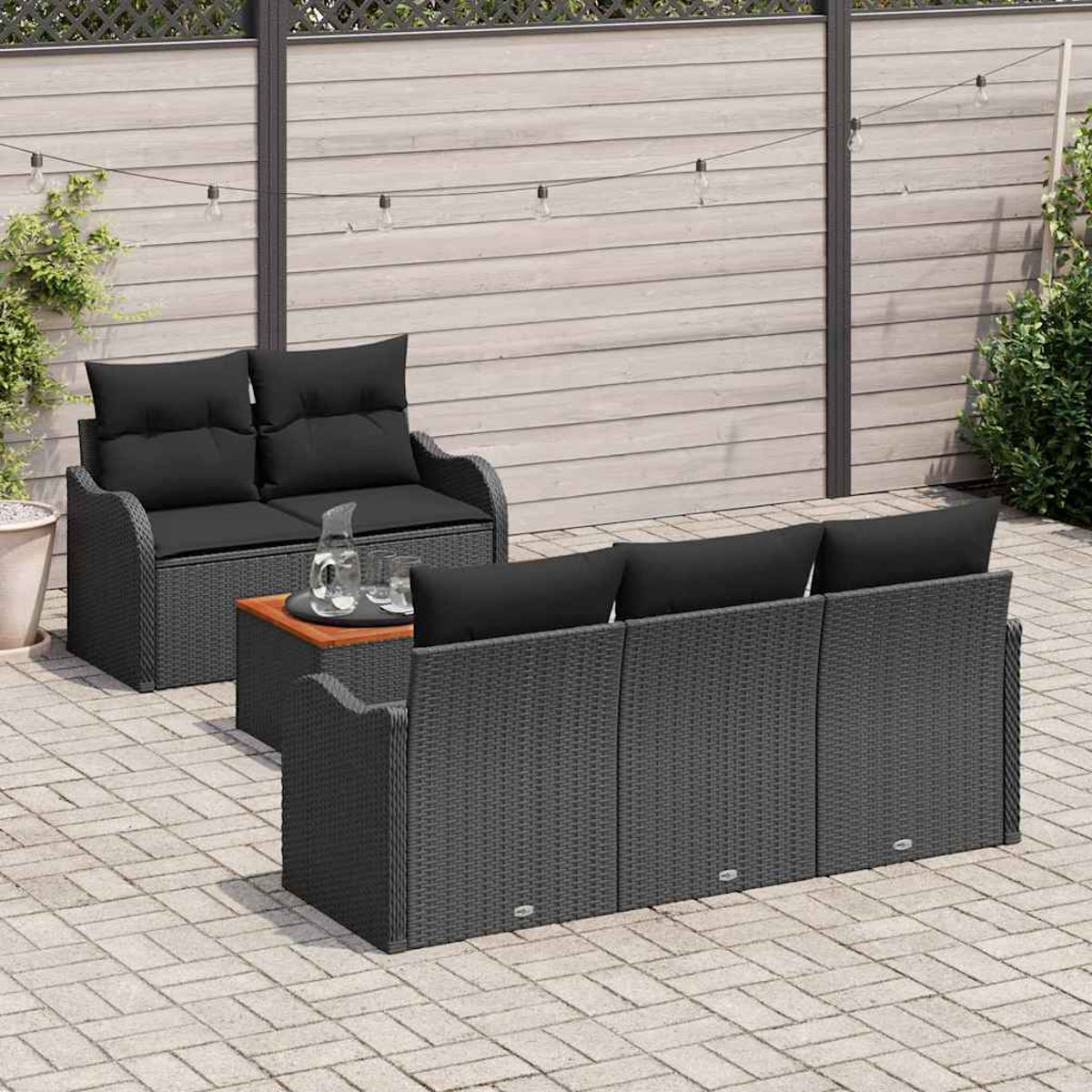 Terrassenset im Freien mit schwarzen Kissen auf grauen Korbmöbeln, einem kleinen Tisch mit Gläsern und einem Holzzaun im Hintergrund.