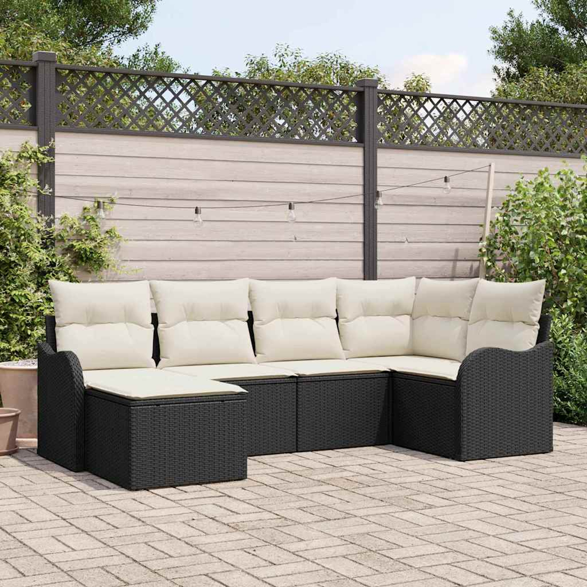 Schwarzes Outdoor-Ecksofa aus Korbgeflecht mit cremefarbenen Kissen auf einer Ziegelstein-Terrasse. Holzzaun und Grün im Hintergrund.