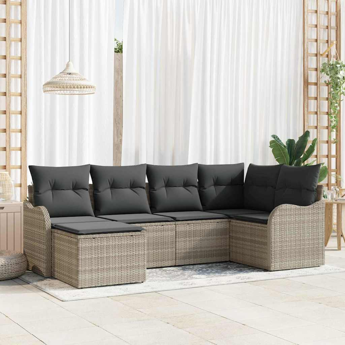 Ein geflochtenes Outdoor-Ecksofa mit grauen Kissen steht auf einem Teppich. Weiße Vorhänge sind im Hintergrund. Eine Hängelampe ist darüber.