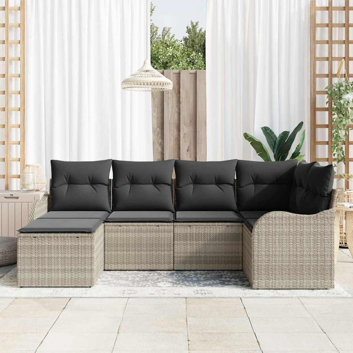 Geflochtenes Outdoor-Ecksofa mit grauen Kissen. Weiße Vorhänge, eine Hängelampe und Pflanzen sind im Hintergrund.