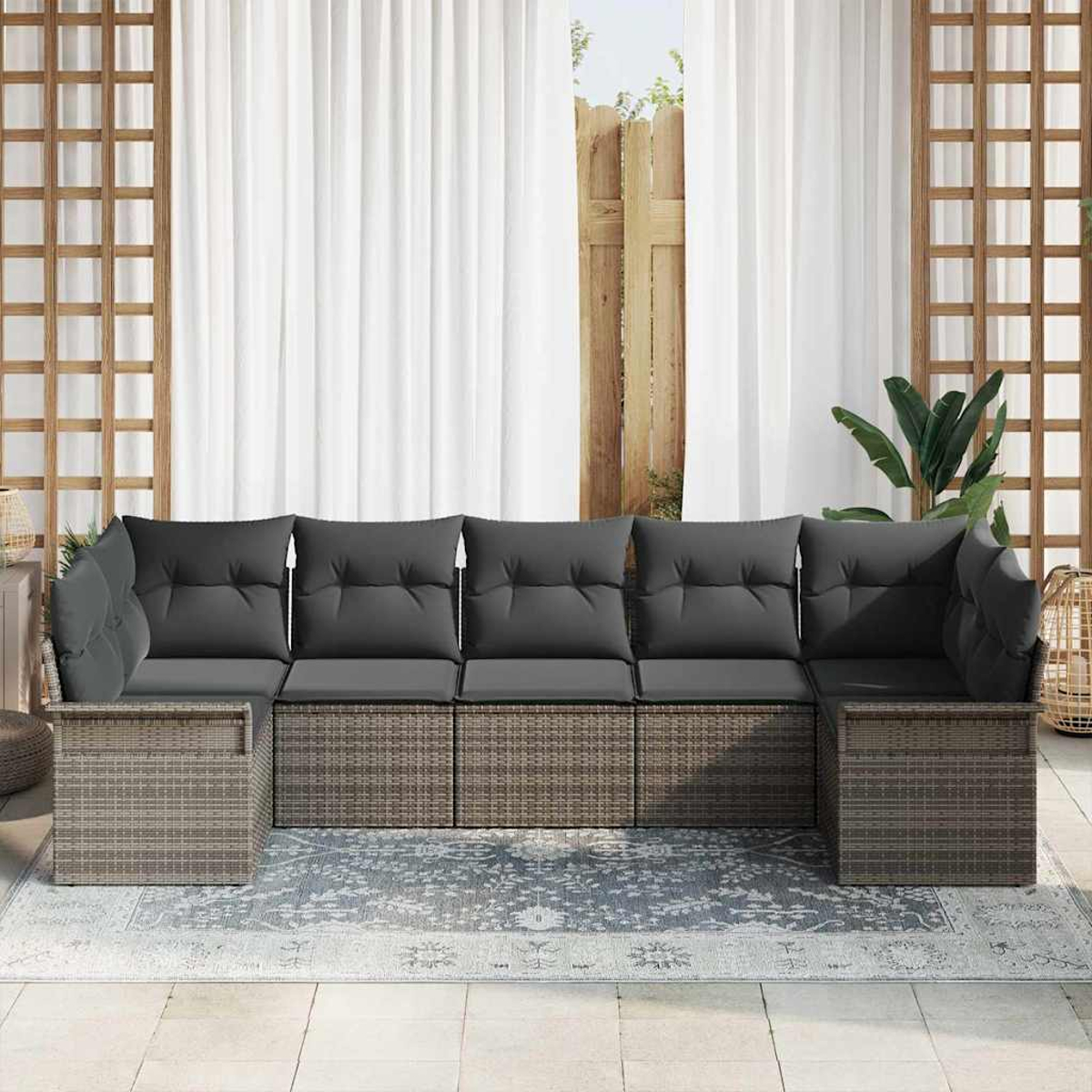 Outdoor-Ecksofa mit grauen Kissen. Dahinter ein weißer Vorhang und ein Holzzaun. Es gibt einen Teppich und einen Korb.