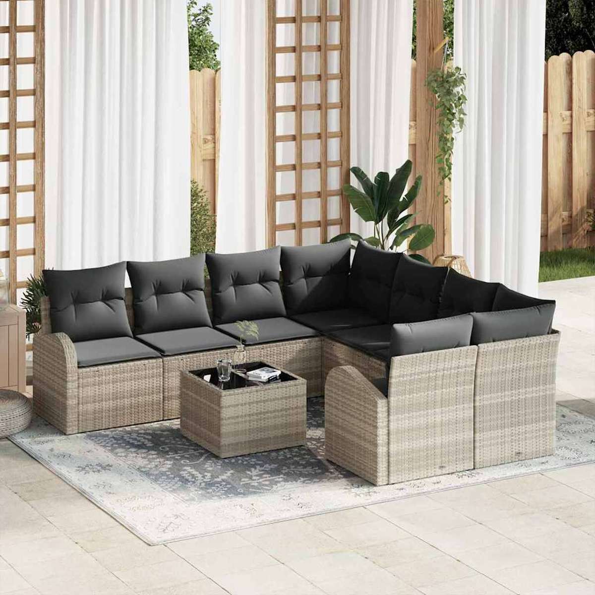 Garten-Sitzgruppe auf einer Terrasse. Sie verfügt über ein Ecksofa mit grauen Kissen, einen kleinen Tisch und einen Teppich. Weiße Vorhänge im Hintergrund.