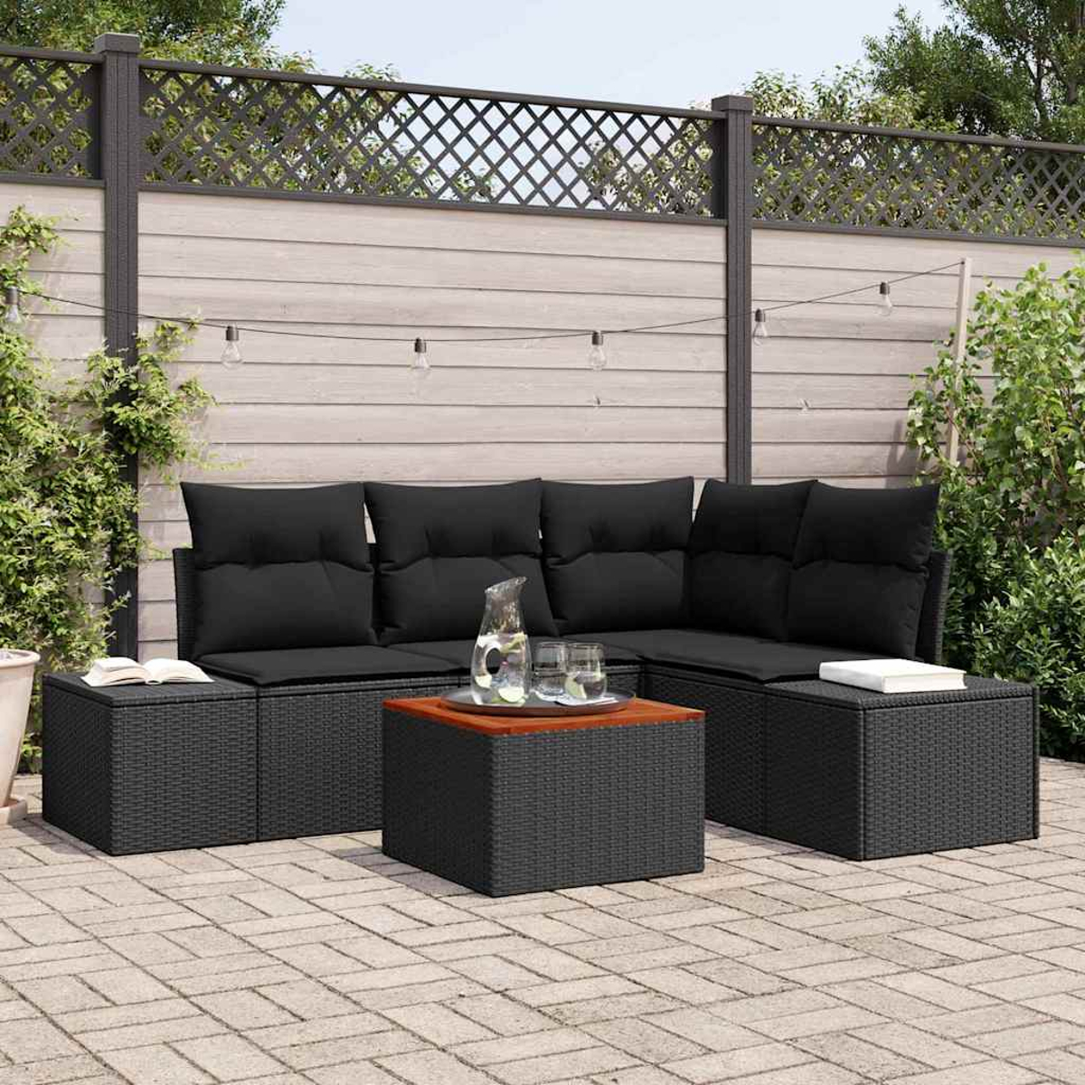 Terrassenset im Freien mit schwarzen Kissen, einem Holztisch und einem Zaun im Hintergrund mit einer Lichterkette.
