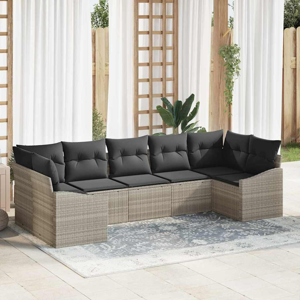 Un sofá exterior en forma de U con cojines gris oscuro se encuentra sobre una alfombra estampada. Cortinas blancas y estructuras de madera.