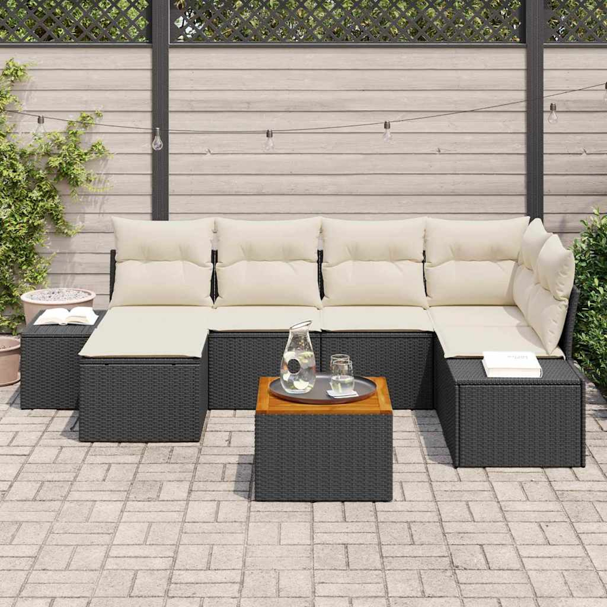 Ein Ecksofa im Freien mit cremefarbenen Kissen. Ein Holztisch mit Wasser und Gläsern steht davor. Im Hintergrund befinden sich ein Zaun und Pflanzen.