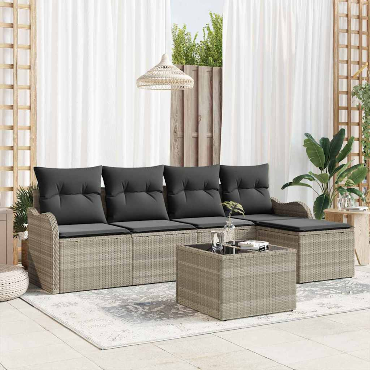 Außenszene mit grauem Rattansofa, Couchtisch und Teppich. Schwarze Kissen, weiße Vorhänge und Pflanzen.