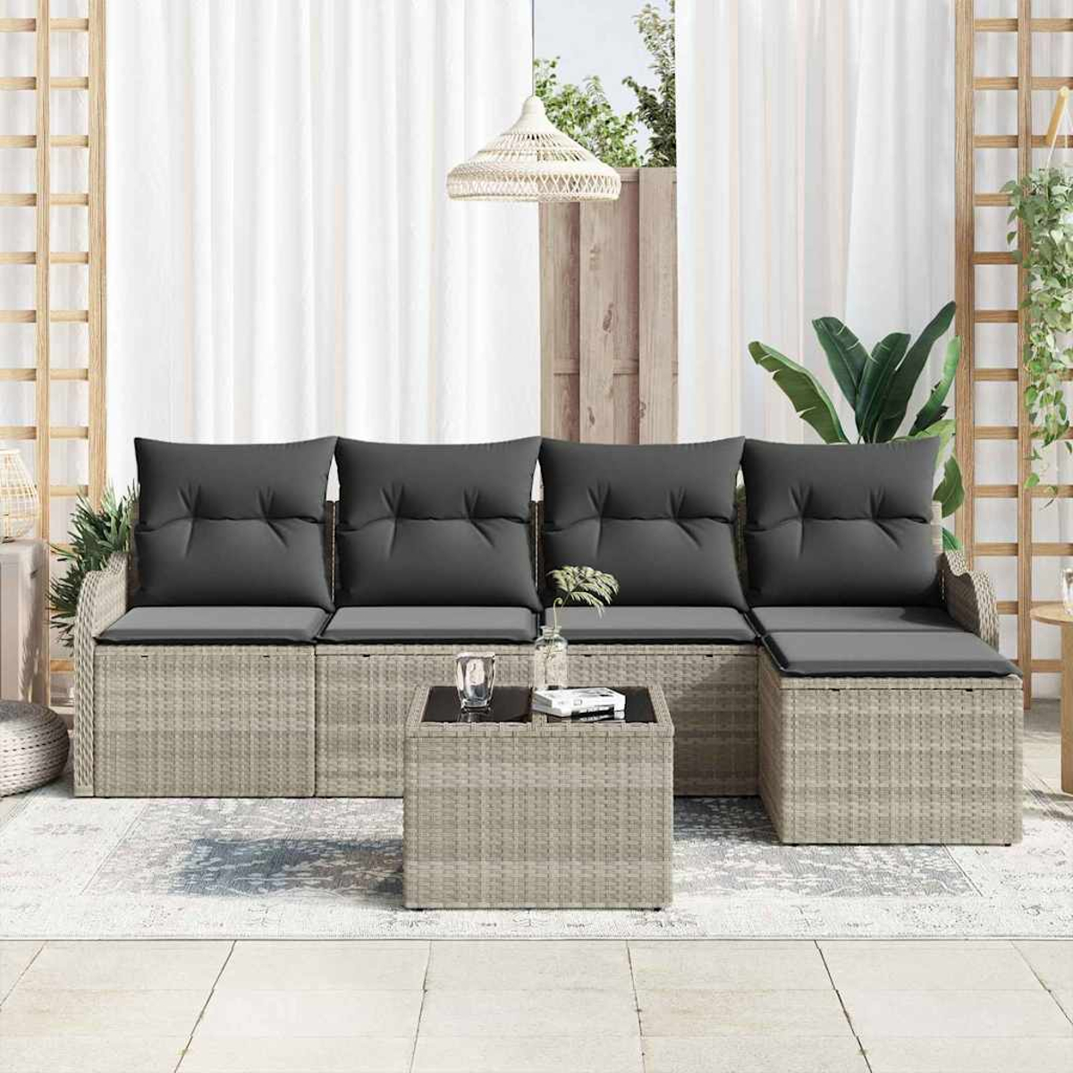 Outdoor-Korbmöbel-Set. Graue Kissen auf dem Sofa und ein quadratischer Tisch mit Glasplatte. Weiße Vorhänge im Hintergrund.