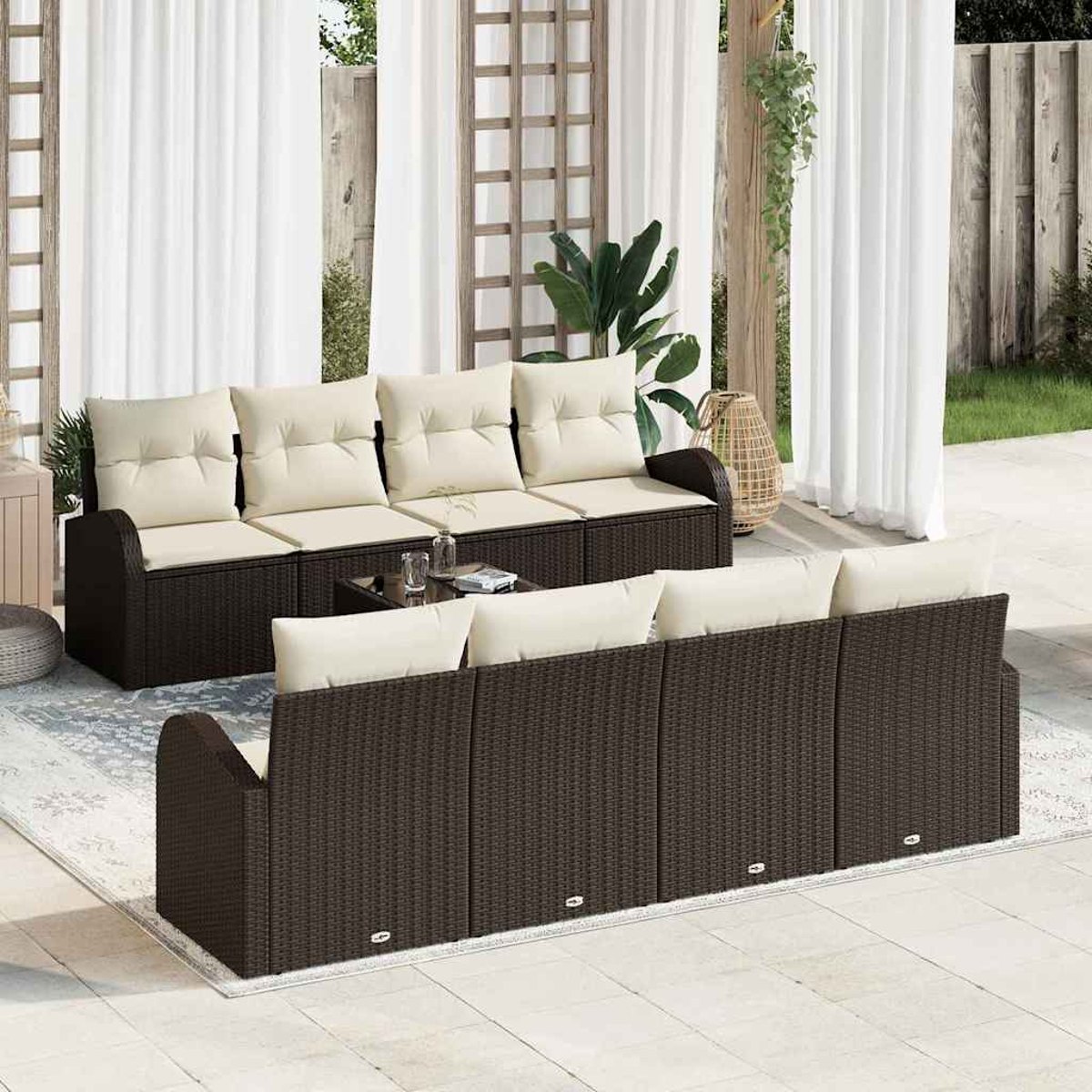 Terrassenset im Freien mit braunen Korbsesseln, cremefarbenen Kissen und einem Glastisch. Weiße Vorhänge und Grün im Hintergrund.