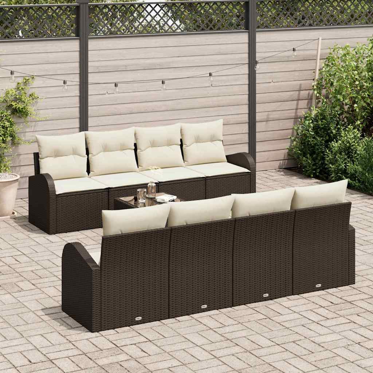 Garten-Set mit braunen Korbsesseln, beigen Kissen und einem kleinen Glastisch. Auf einer Ziegelterrasse mit Holzzaun im Hintergrund.