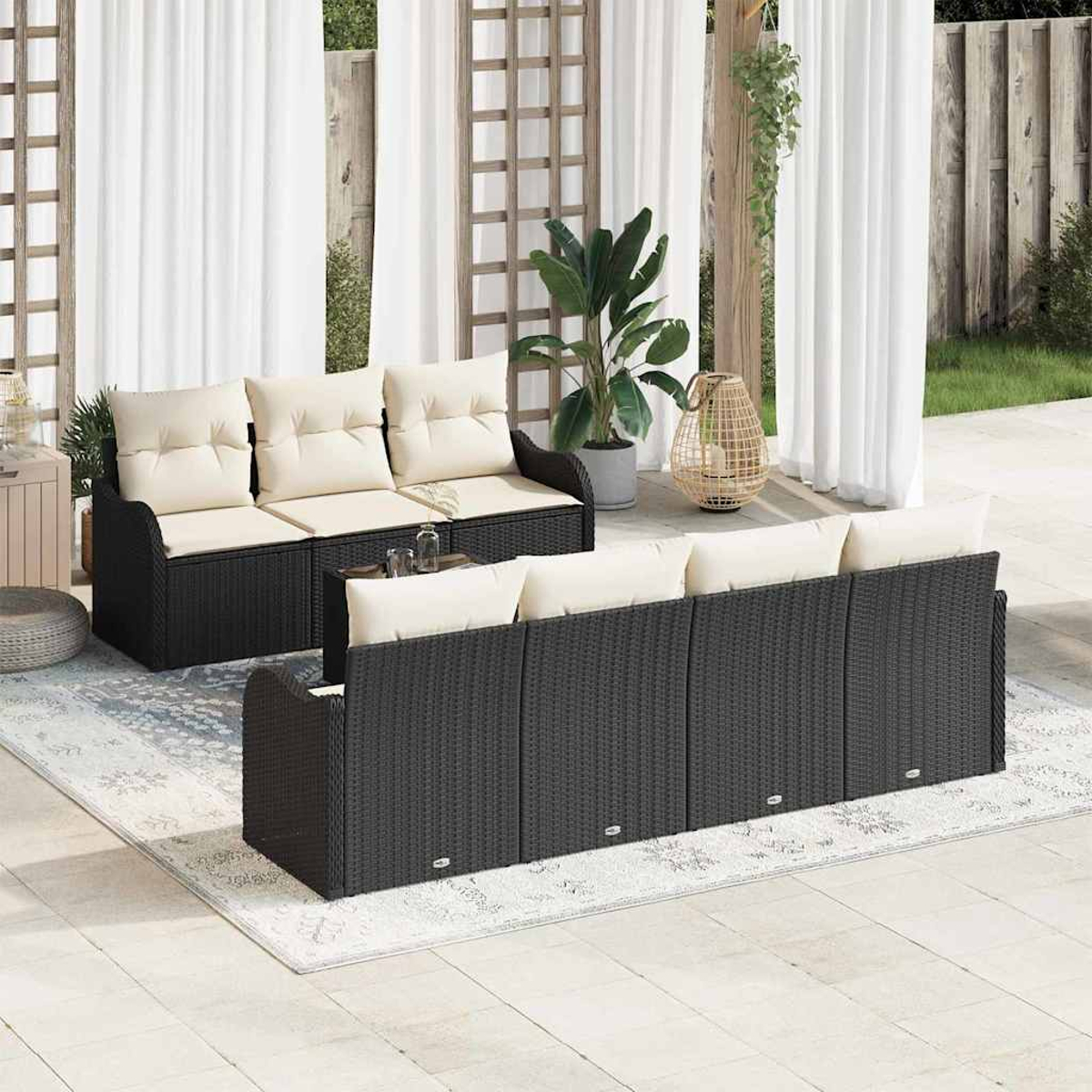 Szene im Freien mit schwarzen Korbs Sofas, cremefarbenen Kissen auf einem Terrassenteppich. Weiße Vorhänge und eine Pflanze im Hintergrund.