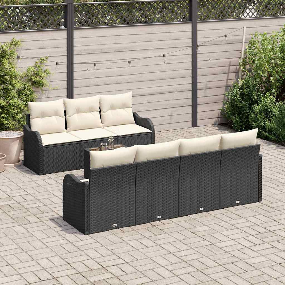 Gartenmöbel-Set. Dunkle Korbsessel mit cremefarbenen Kissen auf einer Steinterrasse, im Hintergrund Zaun und Grün.