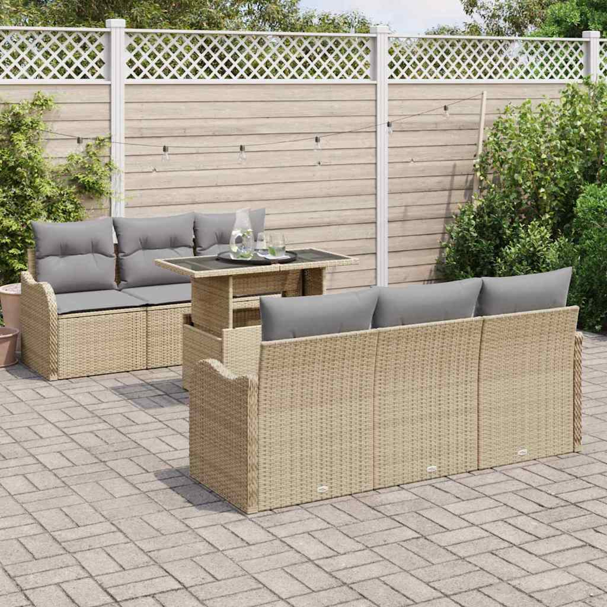 Rattan-Gartenmöbel-Set mit grauen Kissen auf einer Backstein-Terrasse. Ein Tisch mit Getränken steht zwischen den Sofas, im Hintergrund ein Zaun.
