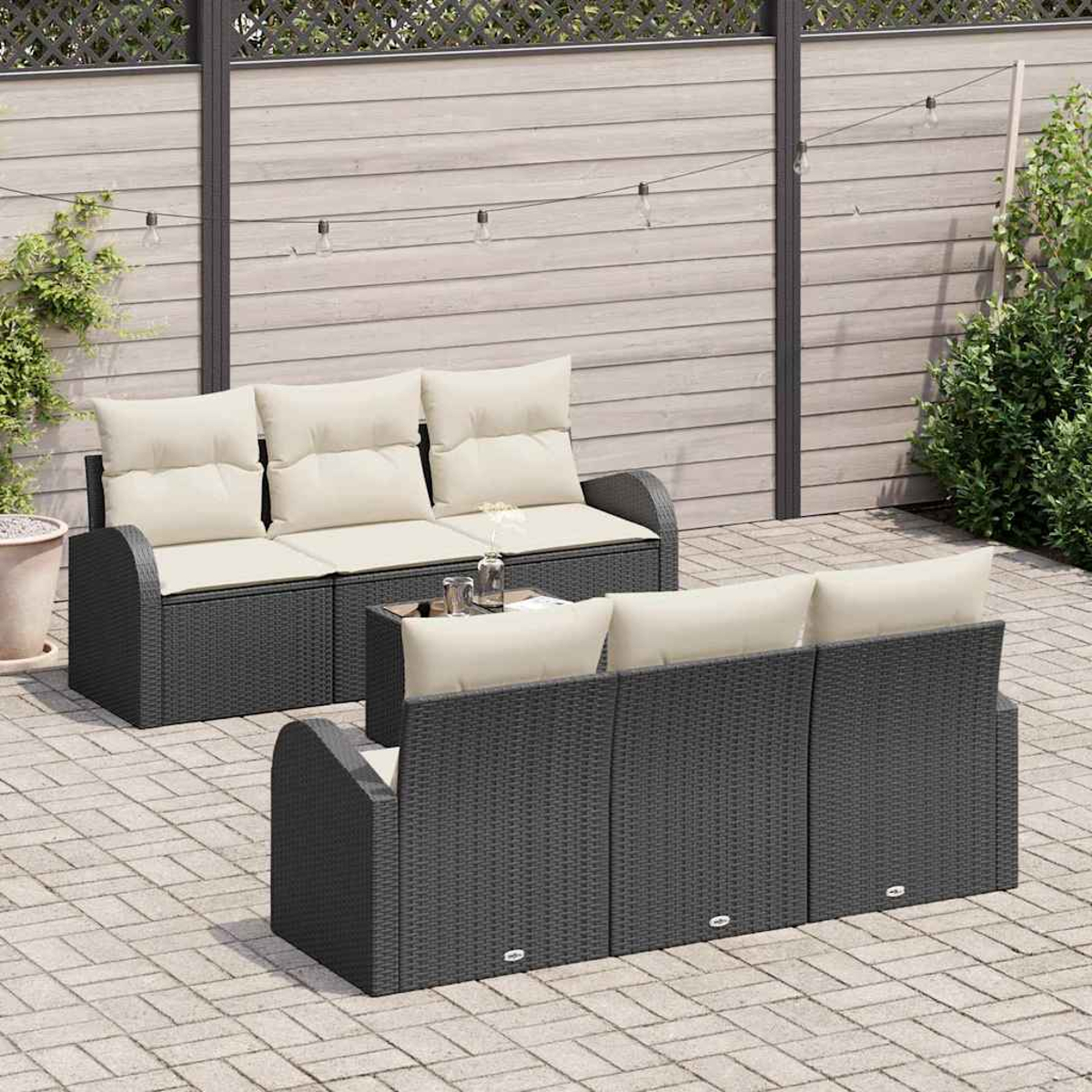 Garten-Sitzgruppe mit dunklen Korbgeweben, beigefarbenen Kissen und einem kleinen Tisch. Auf einer Backstein-Terrasse vor einem Holzzaun mit Lichtern.