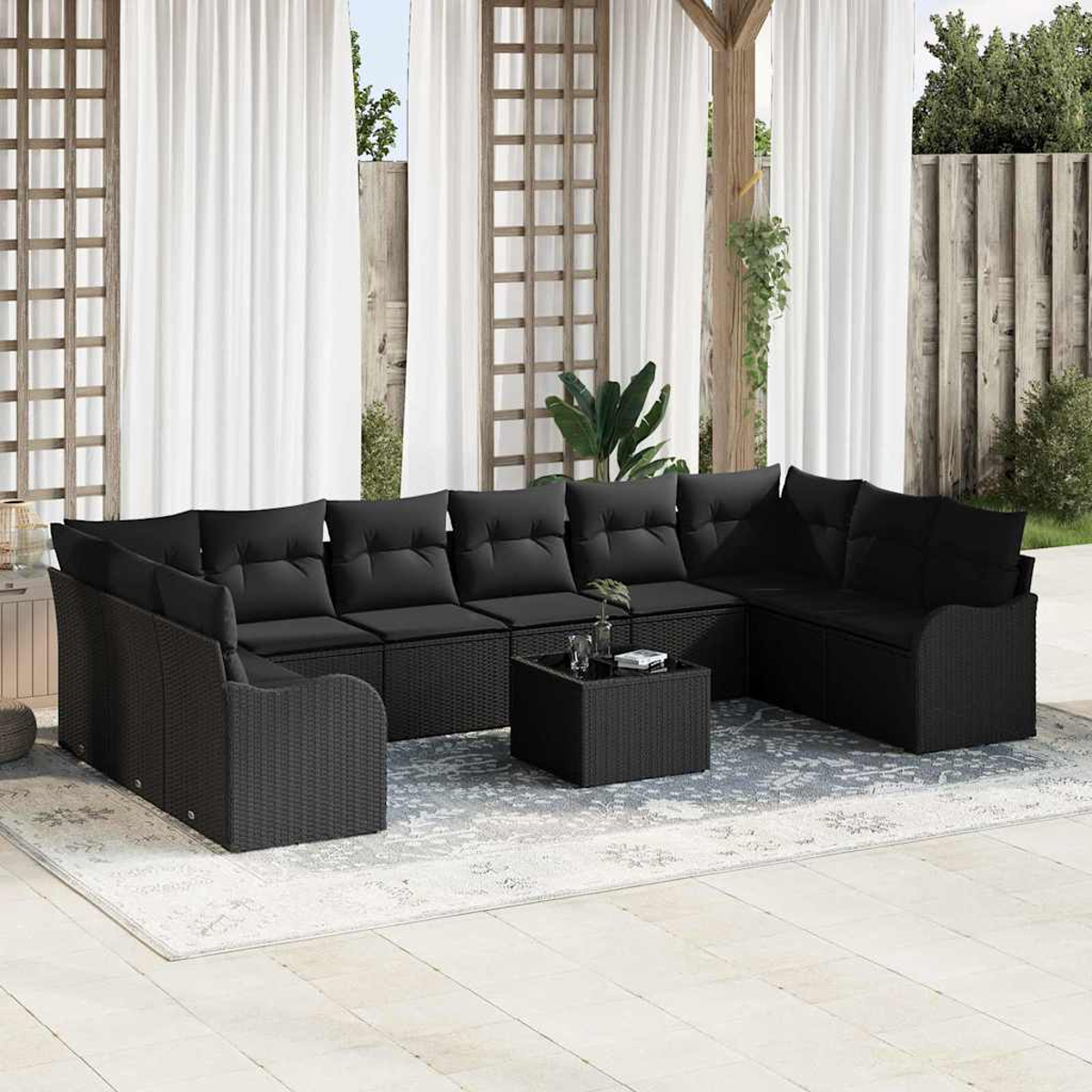 Schwarzes Outdoor-Korfasofa mit Kissen, Couchtisch und Teppich. Weiße Vorhänge und Holzstruktur im Hintergrund.