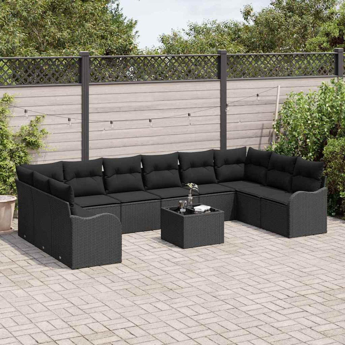 Schwarzes Rattan-Außensektionssofa mit schwarzen Kissen und einem kleinen quadratischen Tisch auf einer Ziegelterrasse, umgeben von einem Zaun.