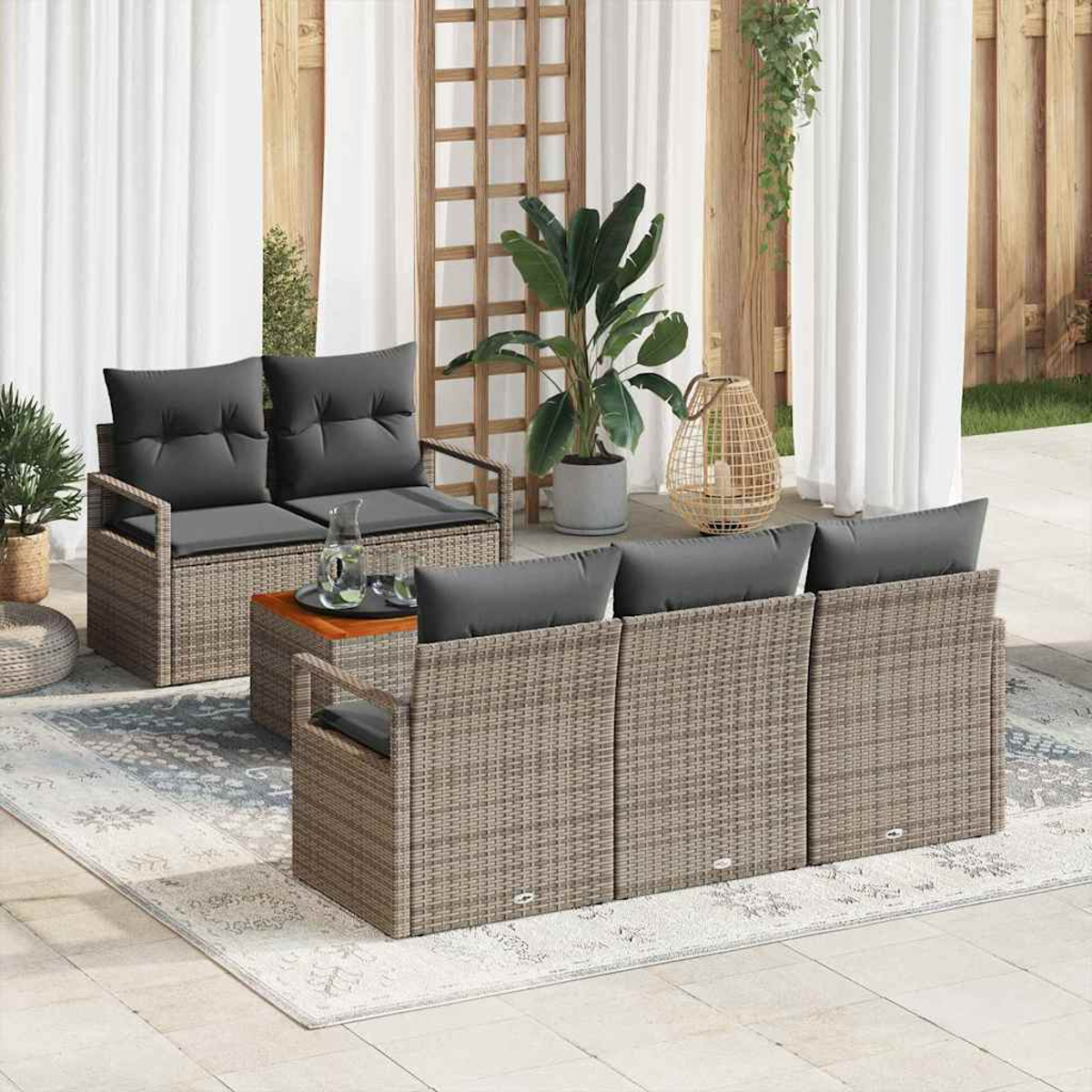 Garten-Terrassenset mit Korbmöbeln, grauen Kissen, einem Holztisch, Teppich, Pflanzen und weißen Vorhängen im Hintergrund.