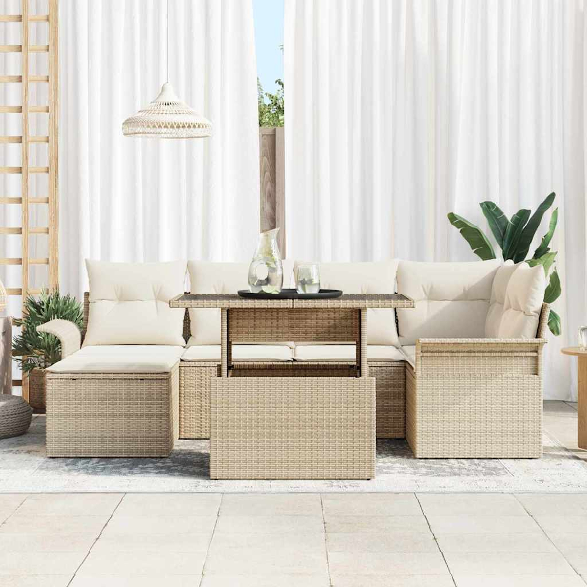 Gartenmöbel-Set aus Korbgeflecht mit Kissen und Tisch. Weiße Vorhänge im Hintergrund. Eine Kanne und Gläser auf dem Tisch.