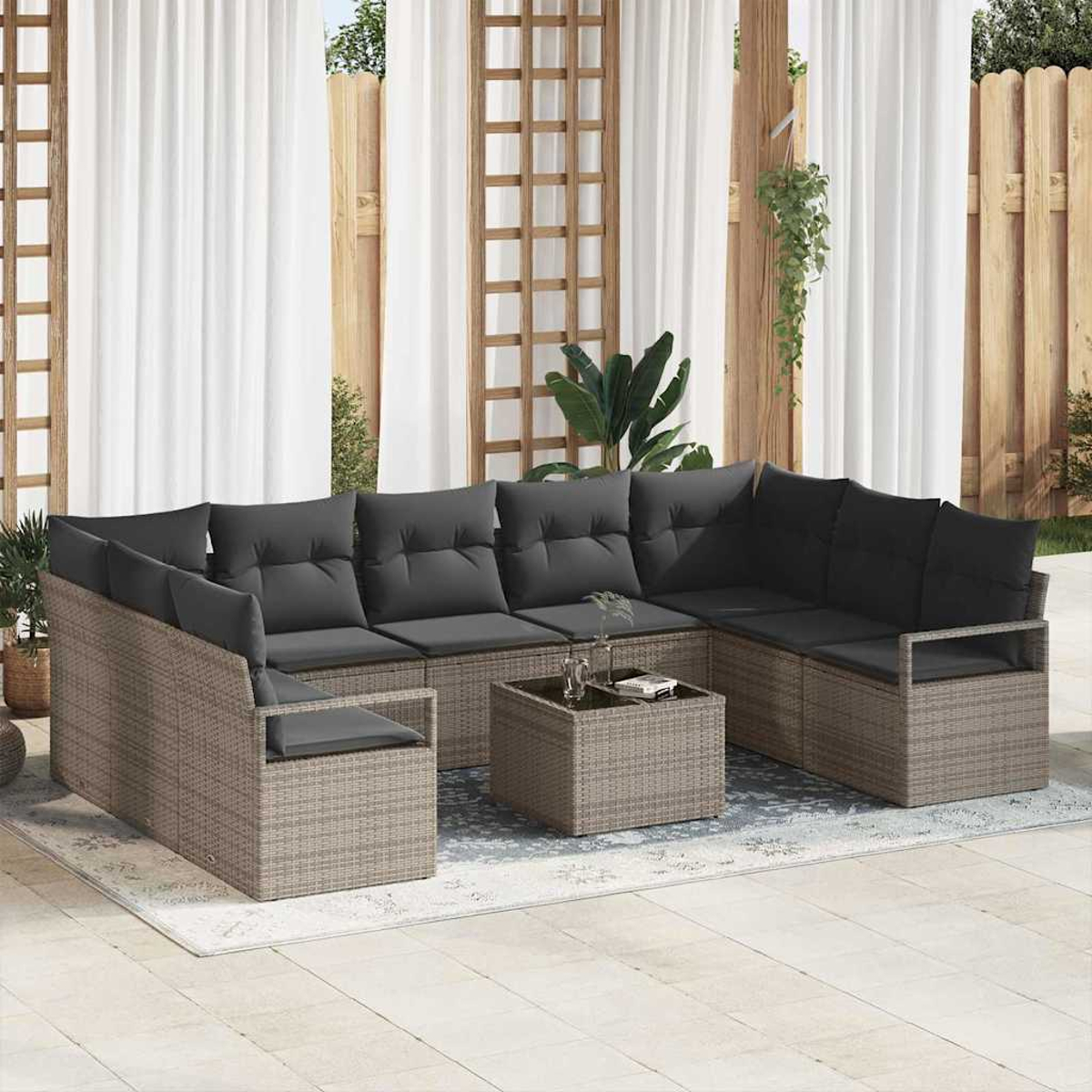 Outdoor-Ecksofa mit grauen Kissen und einem passenden Couchtisch auf einem Teppich. Weiße Vorhänge und Holzzaun im Hintergrund.