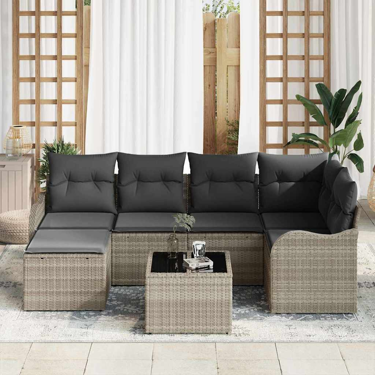 Outdoor-Ecksofa mit grauen Kissen und einem kleinen Tisch auf einer Terrasse. Vorhänge und eine Pflanze im Hintergrund.