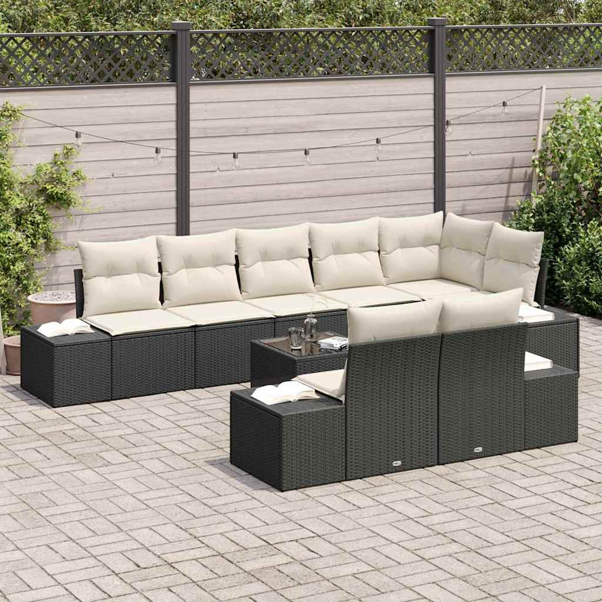 Juego de sofás seccionales para exteriores con cojines crema, mesa de cristal y libros en un patio. Una valla de madera y vegetación al fondo.