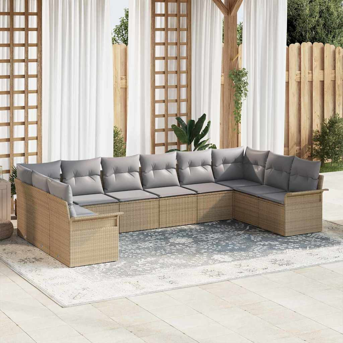 Outdoor-Ecksofa mit grauen Kissen auf einem gemusterten Teppich, vor weißen Vorhängen und einem Holzzaun.