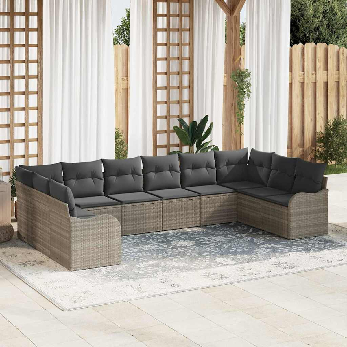 Outdoor-Ecksofa mit grauen Kissen auf einem gemusterten Teppich. Weiße Vorhänge, Holzzaun und Pflanzen im Hintergrund.