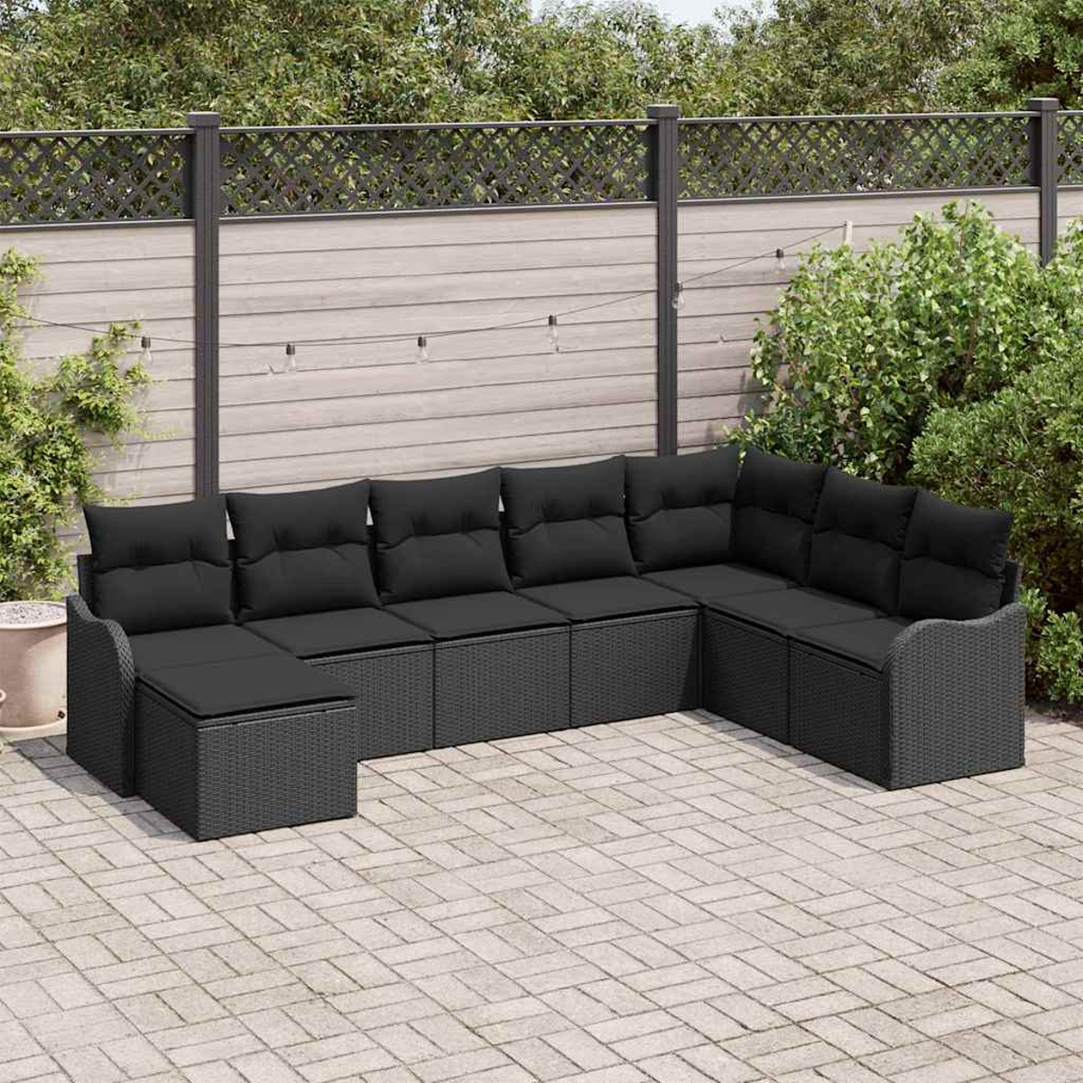 Outdoor-Ecksofa mit schwarzen Kissen auf einer gepflasterten Terrasse. Ein Holzzaun und Grün bilden den Hintergrund.