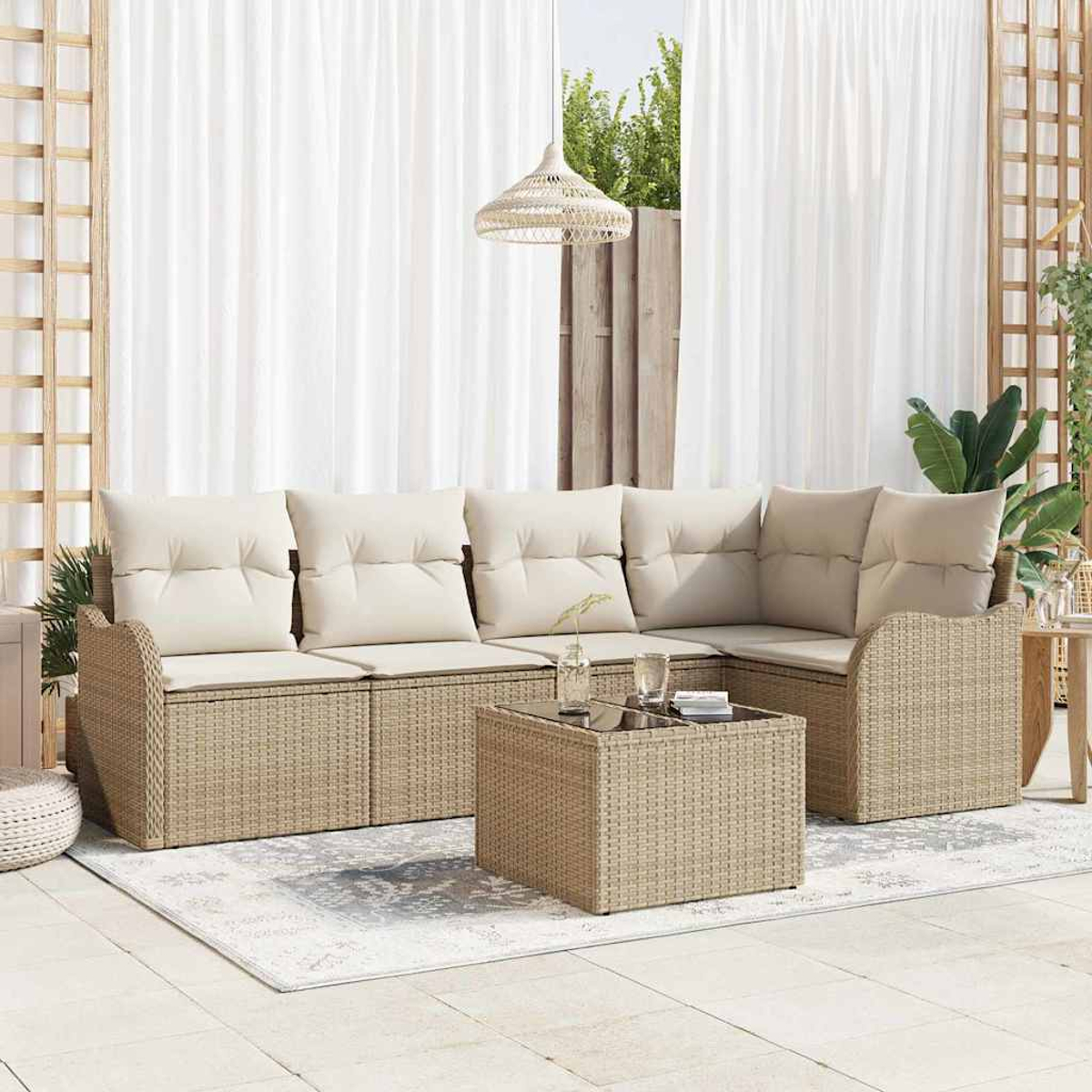 Rattansofa im Freien mit cremefarbenen Kissen und einem Couchtisch. Weiße Vorhänge und eine gewebte Lampe hängen im Hintergrund.