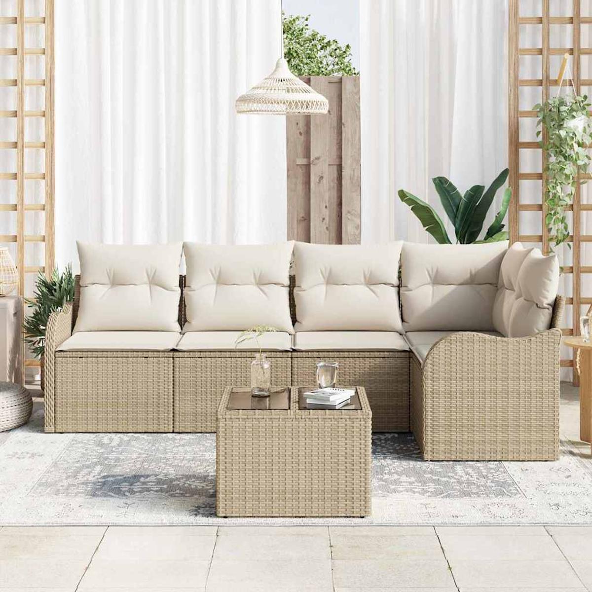 Rattan-Sofa für draußen mit cremefarbenen Kissen, kleinem Tisch mit Glasplatte, weißen Vorhängen, Hängelampe, Teppich und Pflanzen.