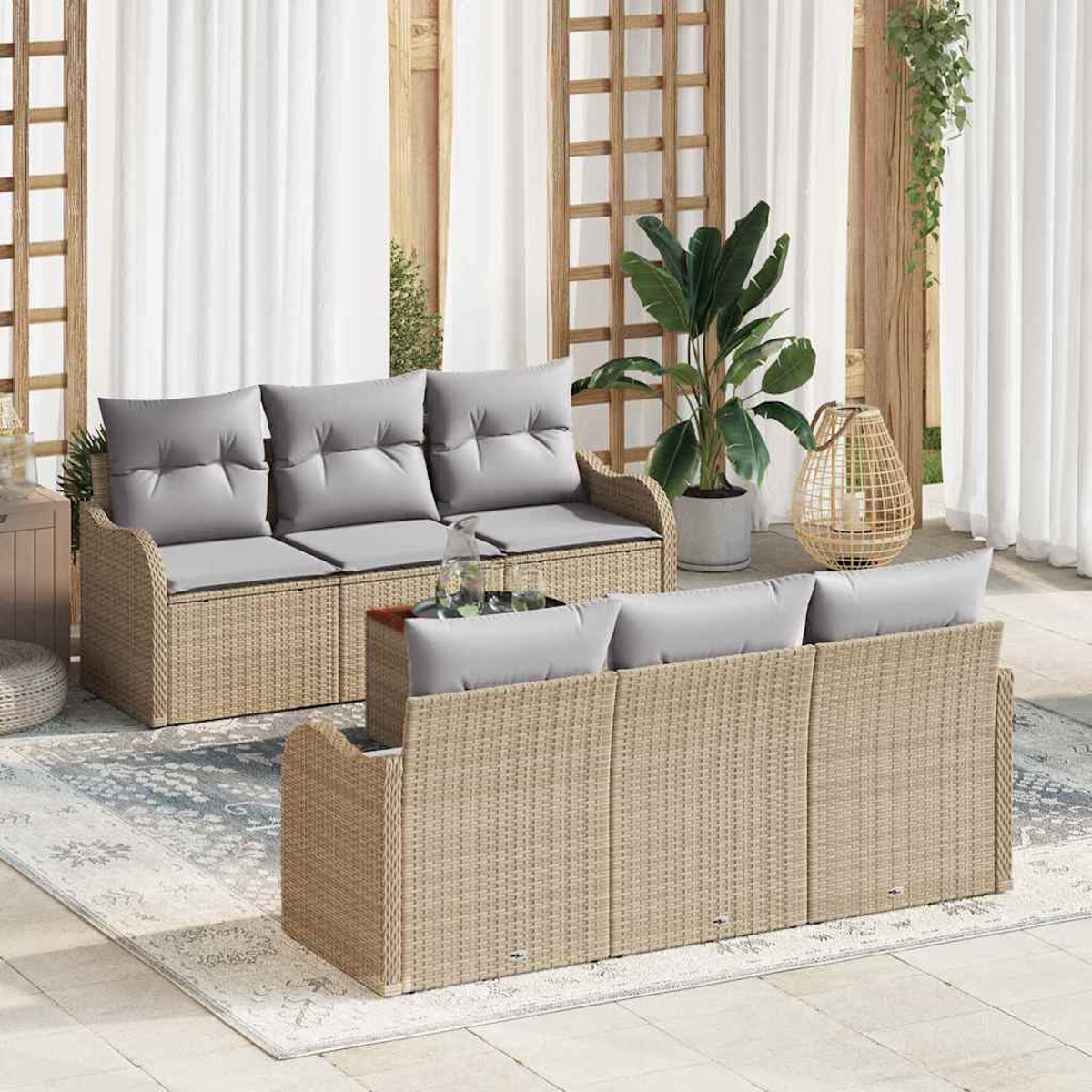 Terrassenset mit Korbs Sofas, grauen Kissen und einem Teppich. Im Hintergrund Pflanzen, Holzgitter und weiße Vorhänge.