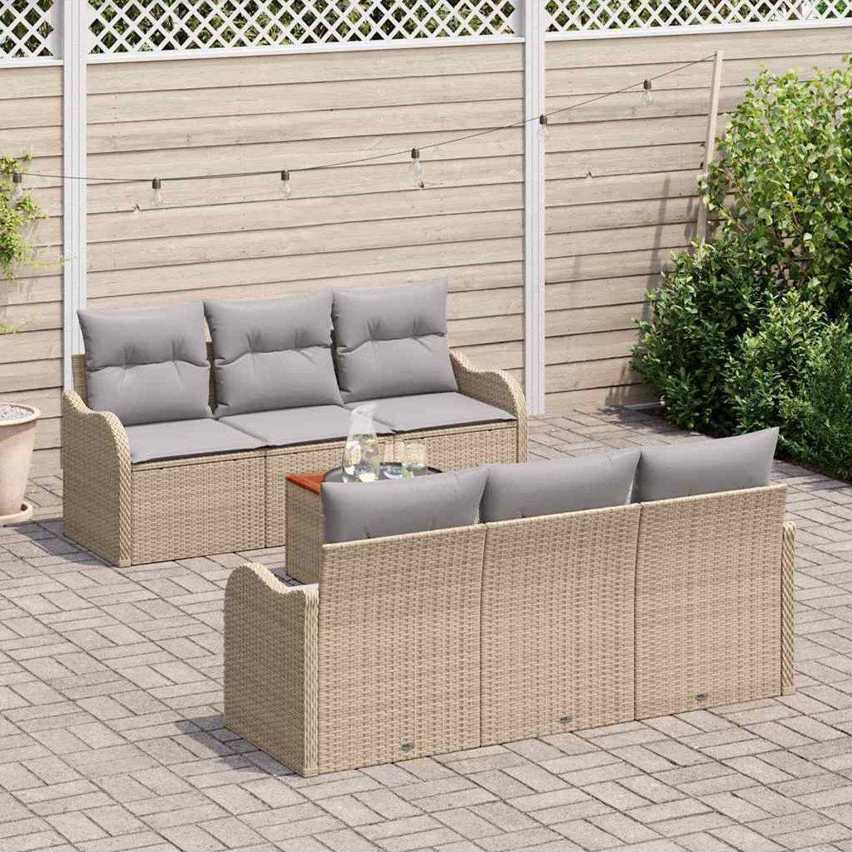 Zwei Korbsessel mit grauen Kissen auf einer Terrasse. Zwischen ihnen steht ein Tisch mit Gläsern und einer Flasche. Holzlattenzaun im Hintergrund.