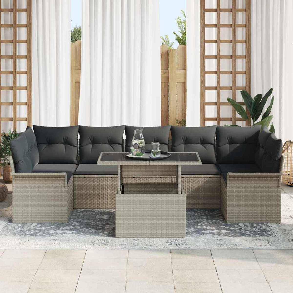 Outdoor-Rattansofa-Set mit grauen Kissen und einem Couchtisch mit Glasplatte. Weiße Vorhänge und Pflanzen im Hintergrund.
