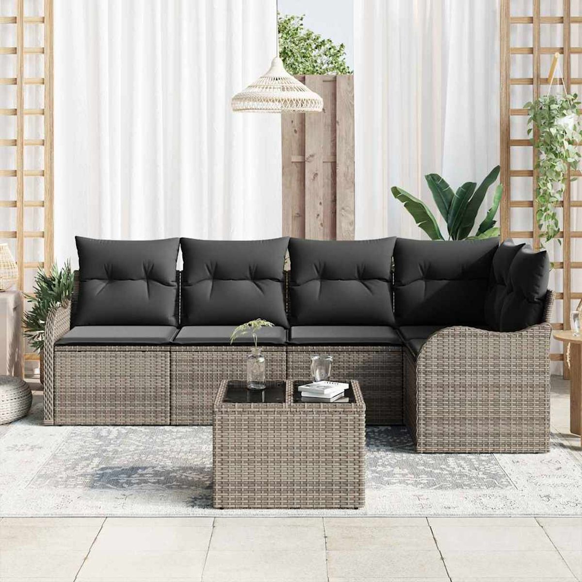 Garten-Sitzgruppe mit grauen Kissen. Ein Couchtisch mit Glasplatte steht davor. Weiße Vorhänge und Pflanzen sind im Hintergrund.