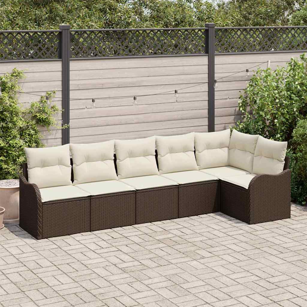 Outdoor-Ecksofa mit cremefarbenen Kissen auf einer Ziegelterrasse. Im Hintergrund ein Zaun und Grün. Über dem Sofa befinden sich Lichterketten.