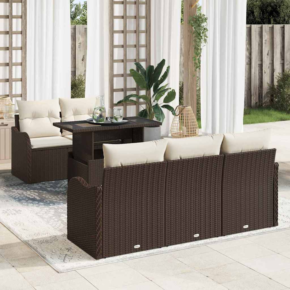 Garten-Set mit braunen Korbmöbeln, cremefarbenen Kissen, einem Tisch mit Tablett und einem Teppich, mit weißen Vorhängen im Hintergrund.