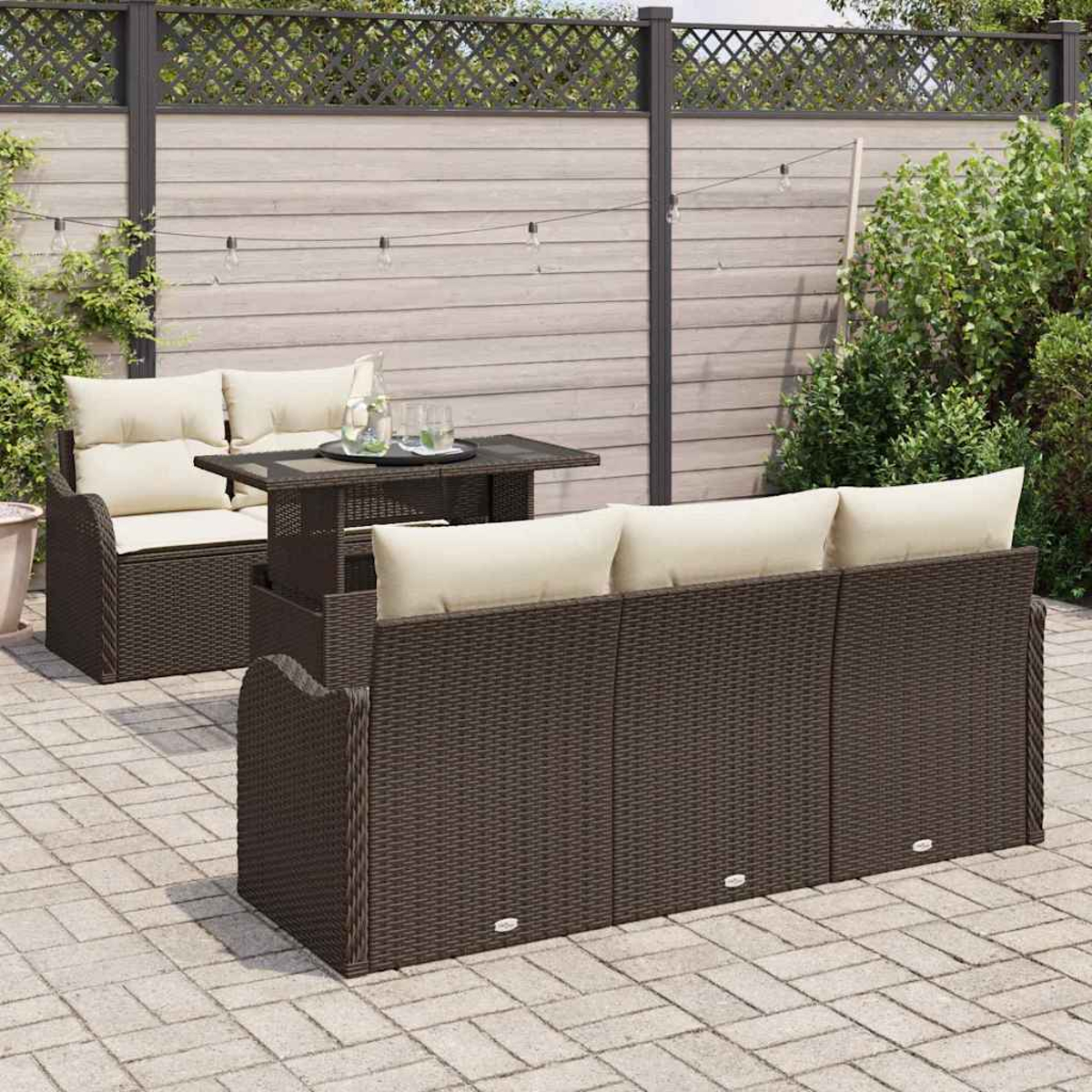 Gartenmöbel-Set: braunes Korbmöbel-Sofa und -Liege mit cremefarbenen Kissen, ein Tisch mit Getränken und ein Holzzaun im Hintergrund.