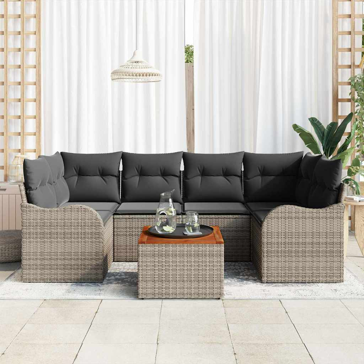 Ein moderner Sitzbereich im Freien mit grauen Kissen, einem Holztisch und einem gewebten Rattan-Design. Weiße Vorhänge und eine Hängelampe sind sichtbar.