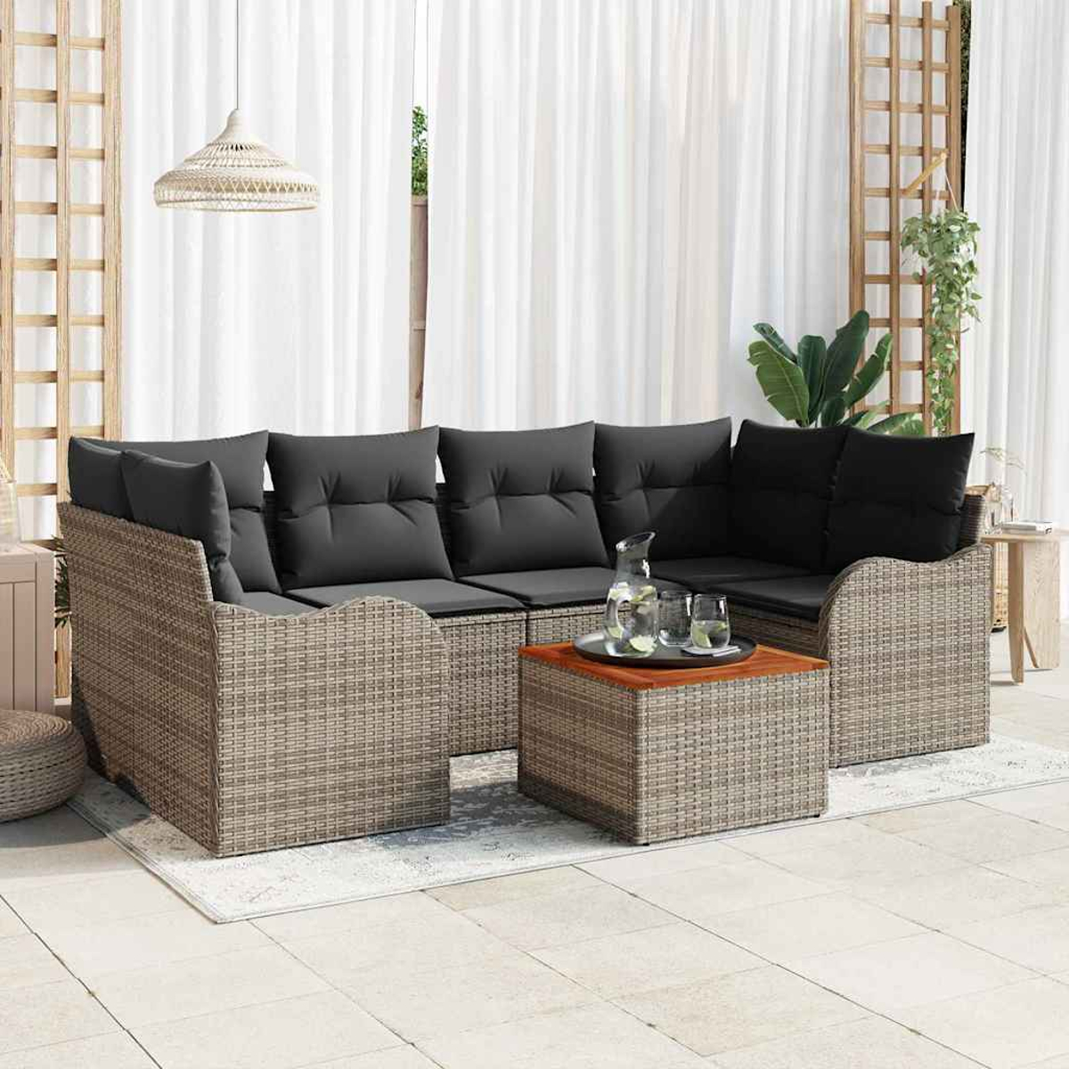 Outdoor-Ecksofa mit grauen Kissen, einem hölzernen Couchtisch und einem Wasserkrug. Weiße Vorhänge im Hintergrund.