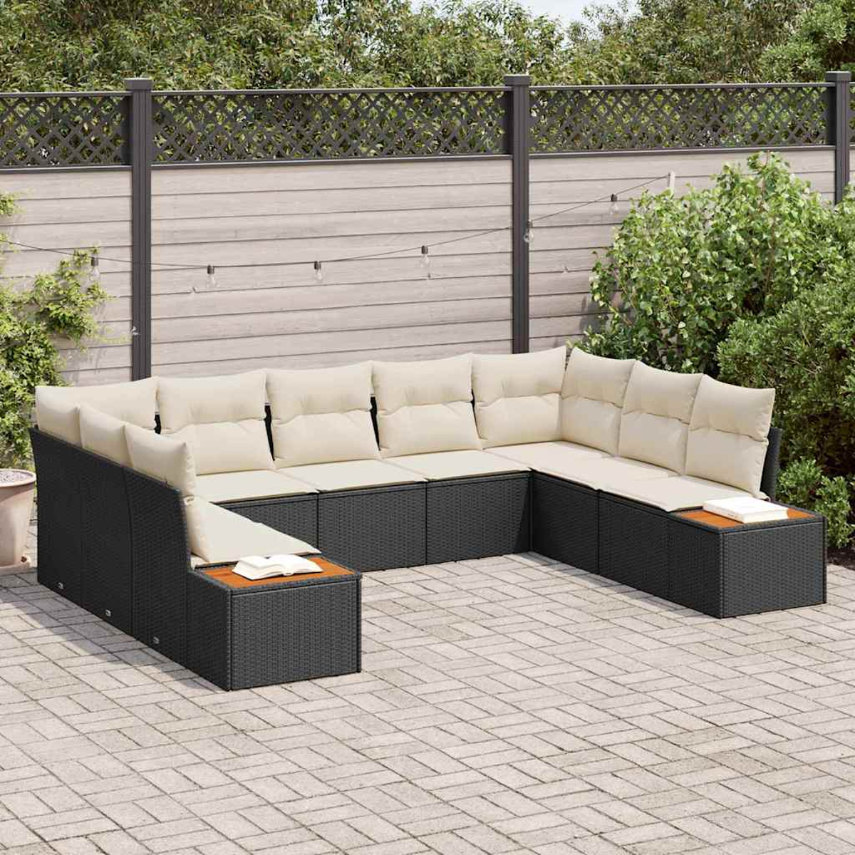 Outdoor-Ecksofa mit beigen Kissen. Schwarze Korbbasis. Auf einer Backstein-Terrasse, Zaun und Grün im Hintergrund.