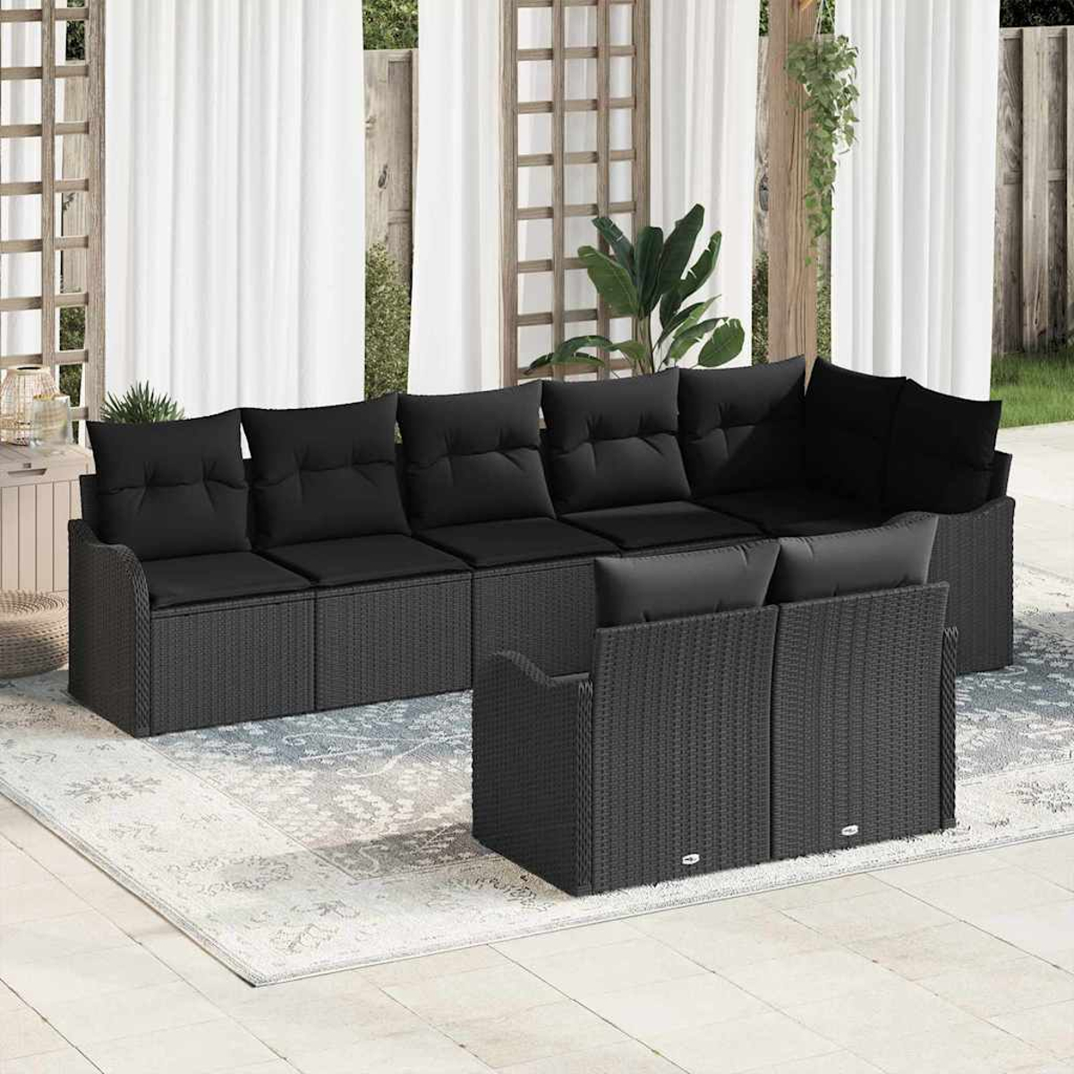 Schwarzes Outdoor-Ecksofa aus Korbgeflecht mit schwarzen Kissen. Sofa steht auf einem gemusterten Teppich auf einer Terrasse. Weiße Vorhänge im Hintergrund.