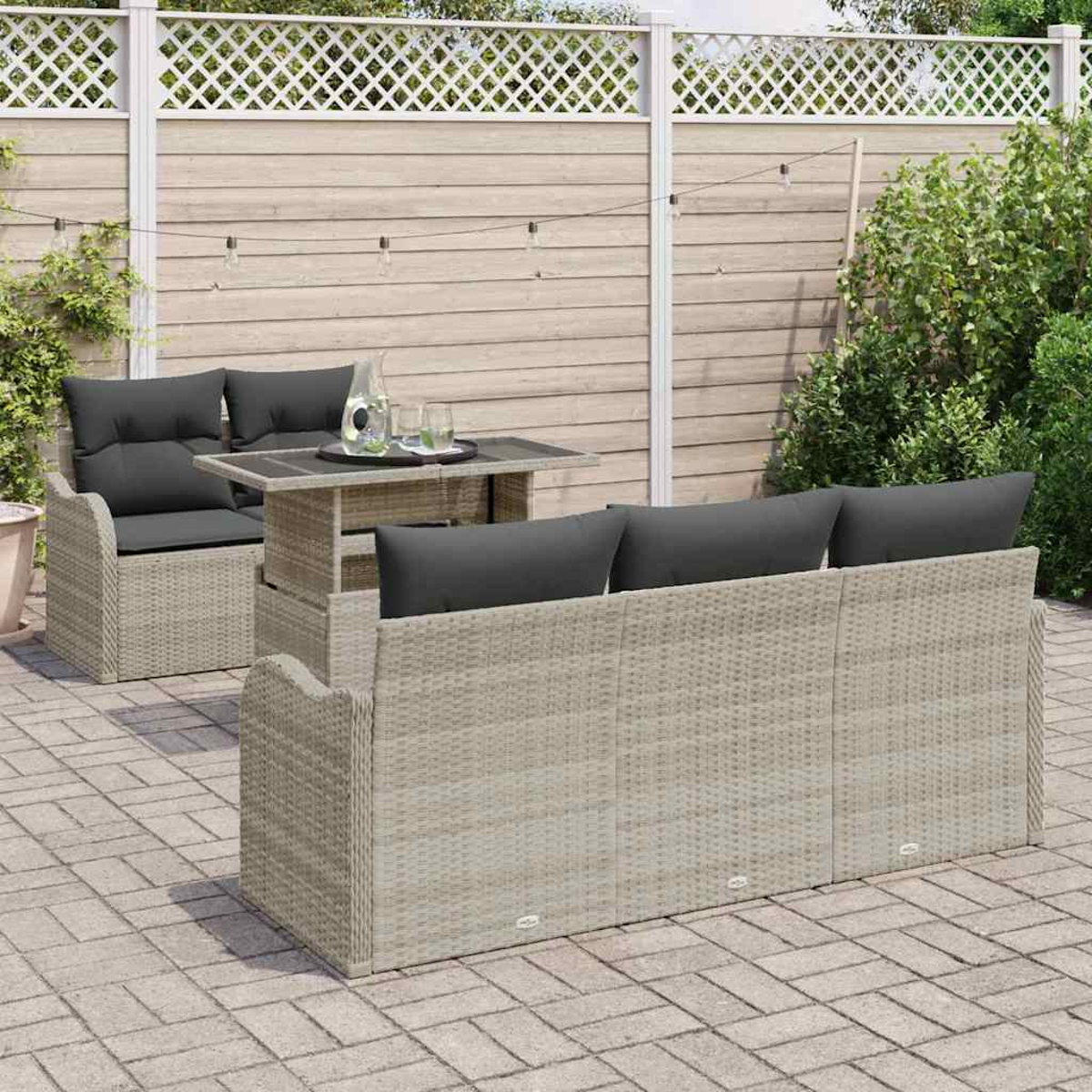 Szene im Freien mit Rattan-Sofa, Tisch und Stühlen. Dunkle Kissen, Glastisch und Holzzaun.