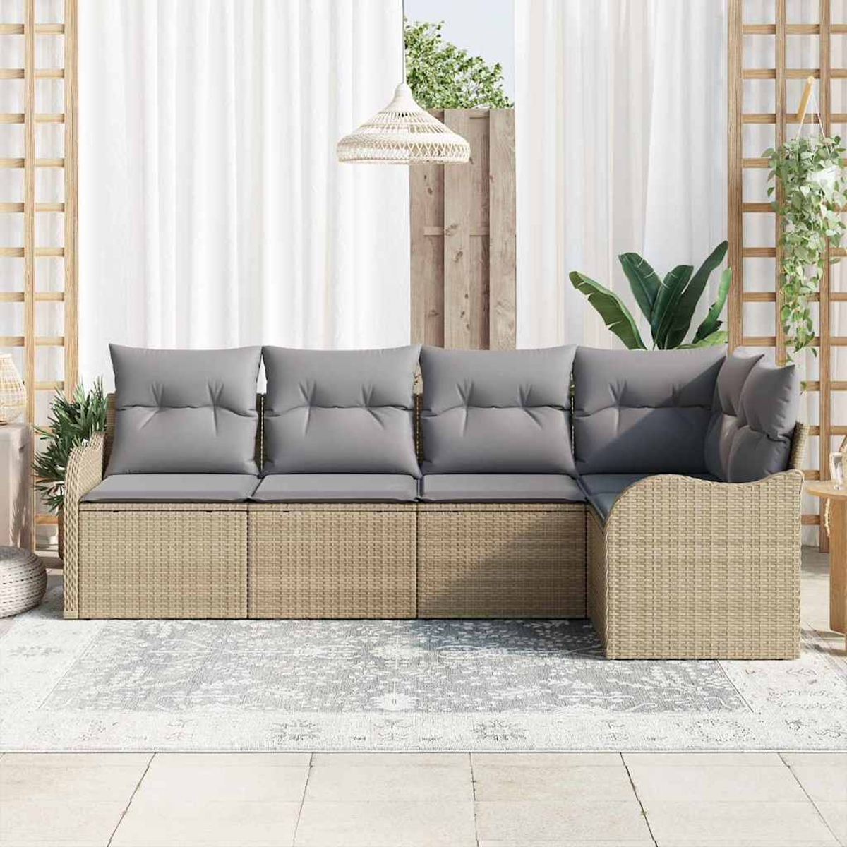 Ein Rattansofa mit grauen Kissen steht auf einem Teppich. Weiße Vorhänge und eine Hängelampe sind im Hintergrund. Pflanzen sind ebenfalls zu sehen.