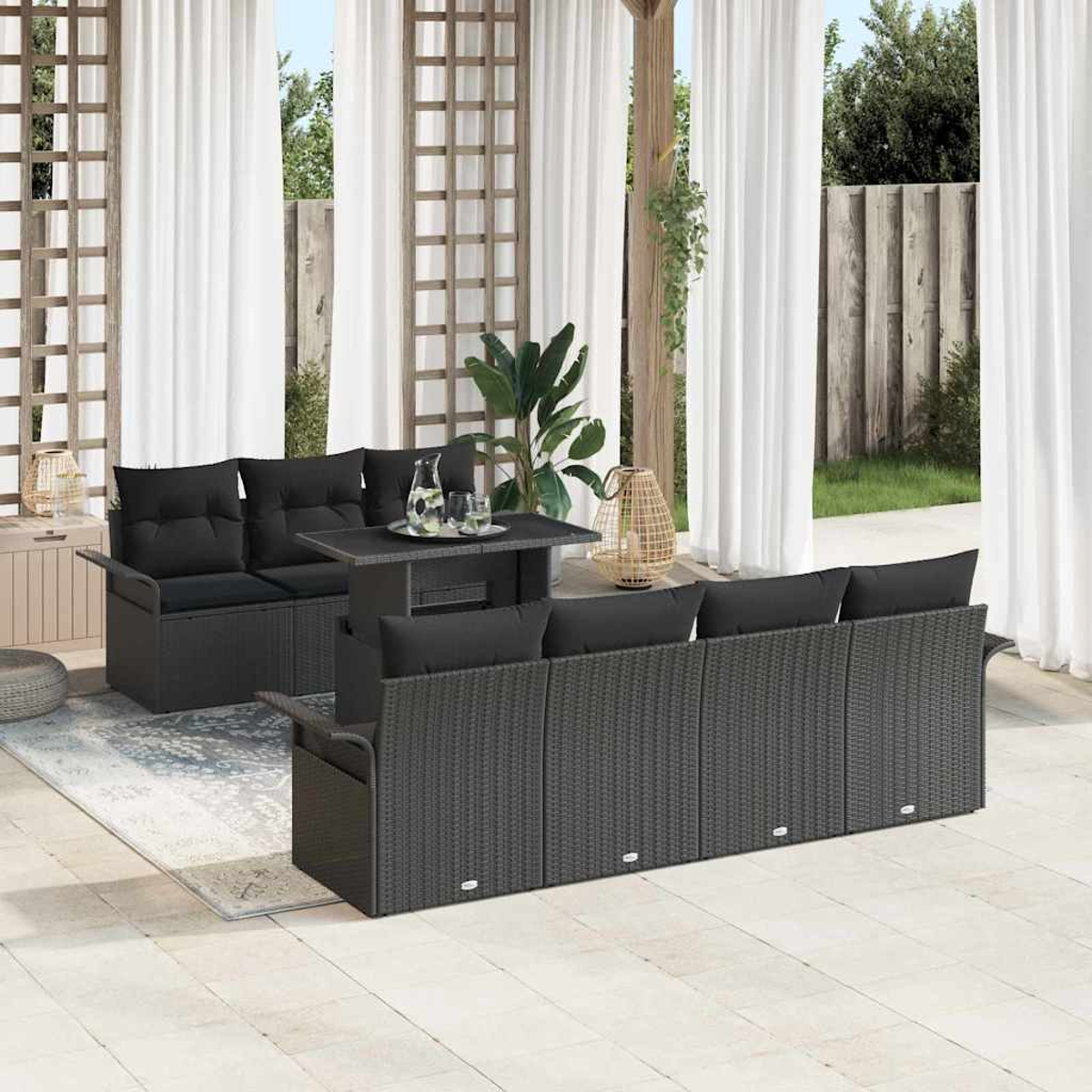 Terrassenset mit schwarzen Rattansofas, Tisch und Kissen. Weiße Vorhänge und Grün im Hintergrund. Sonniger Tag.