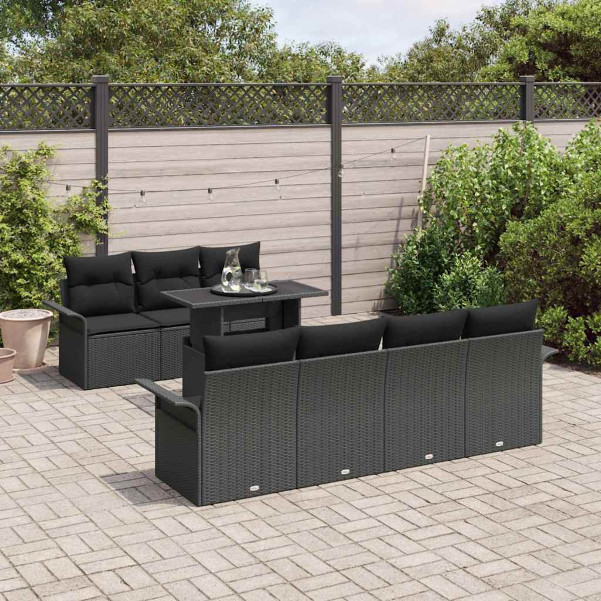 Terrassenset mit schwarzen Kissen. Enthält ein Sofa, eine Couch, einen Tisch und einen Hintergrund aus Grün und einem Zaun.