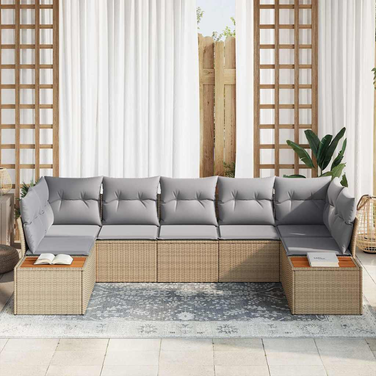 Ein U-förmiges Sofa aus Korbgeflecht mit grauen Kissen steht auf einem gemusterten Teppich vor einem Fenster mit weißen Vorhängen.