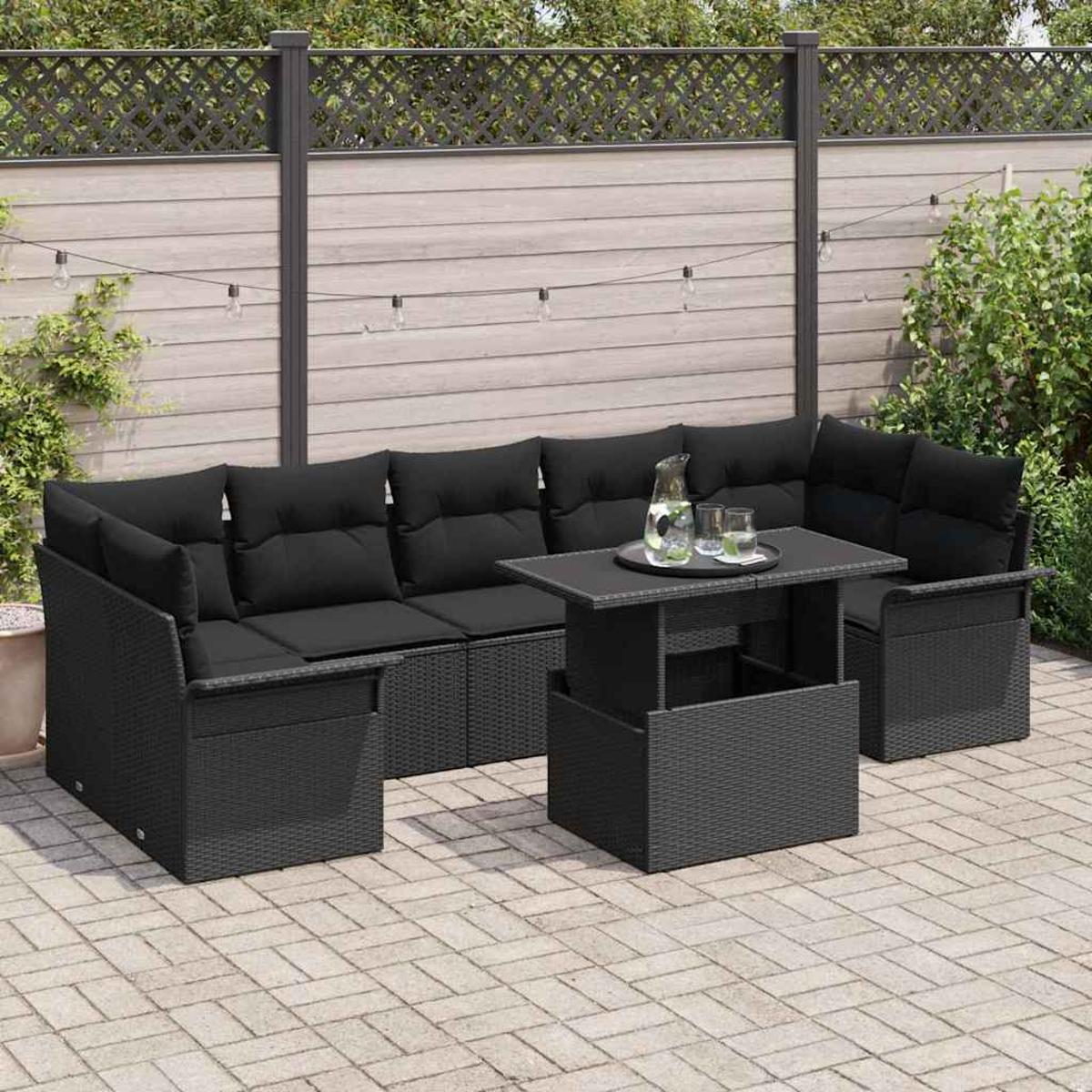 Ein schwarzes Outdoor-Ecksofa und ein Couchtisch mit Kissen auf einer Ziegelterrasse. Ein Zaun und Grünzeug sind im Hintergrund.